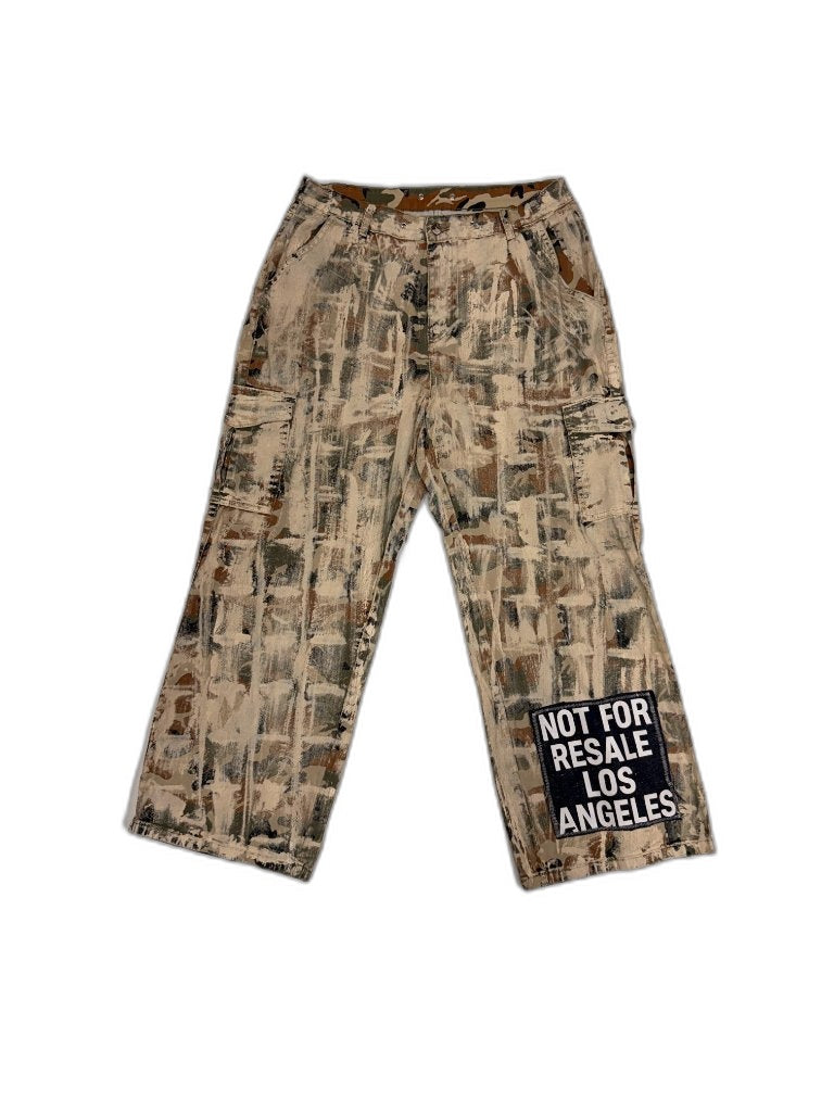 Front of bleached desert camo cargo pants with white paint brushstroke treatment and NOT FOR RESALE LOS ANGELES sewn patch on right leg — one of one upcycled reconstructed streetwear Los Angeles