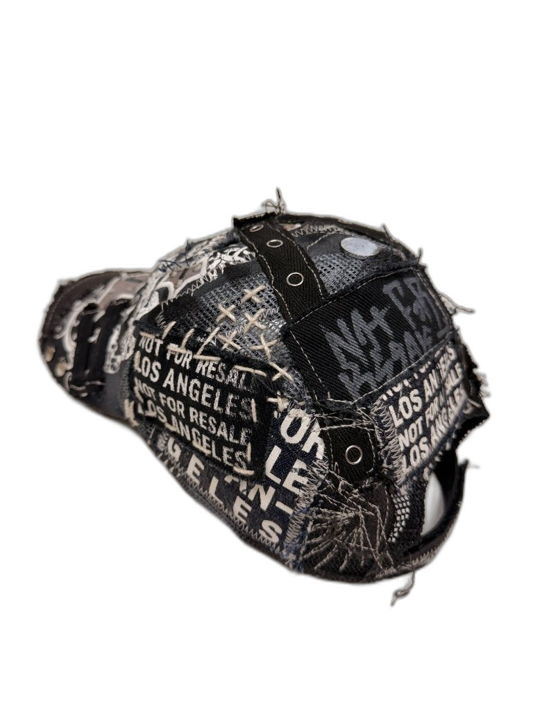 Side view of black skull cap showing X webbing crown construction grommets skull print panels and raw frayed seams — one of one upcycled NFR LA