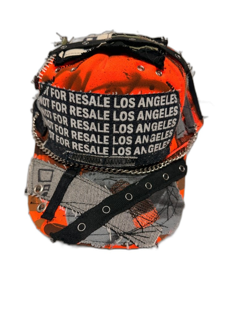 Front of orange camo cap with NOT FOR RESALE LOS ANGELES repeating woven text band wrapping crown silver chain on bill and black grommet strap — one of one NFR LA