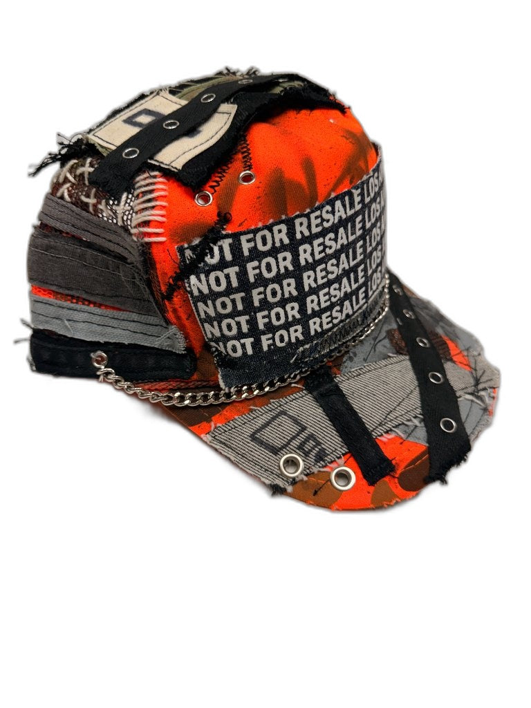 Side view of orange camo cap showing NFR text band silver chain grommet strap layered grey fabric strips and white cross stitch — one of one reconstructed Not For Resale