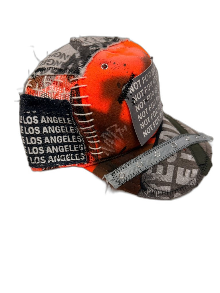 Side of orange spray cap showing LOS ANGELES woven text patch NFR stencil white ladder stitching grommet strap on bill and orange mesh panels — one of one reconstructed Not For Resale