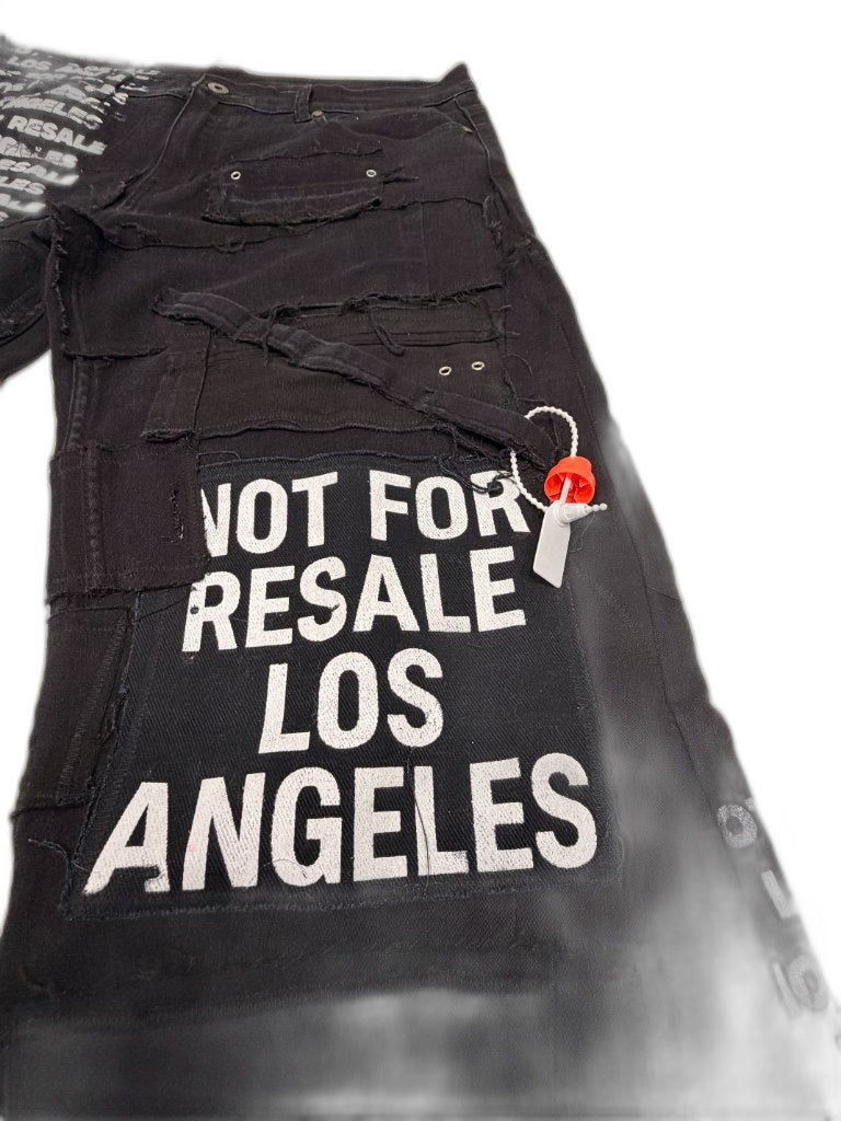 Close detail of NOT FOR RESALE LOS ANGELES large sewn patch on thigh with red hang tag grommets and raw frayed deconstructed seam panels — one of one upcycled NFR LA